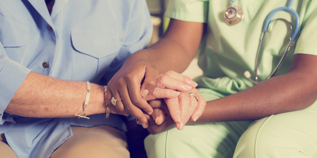 Caring home healthcare nurse conducts medical consultation with senior adult woman at her home or nursing home. The elderly female patient is being comforted by the African descent nurse as she is holding her hands as they talk together. Focus on hands. Vintage look.