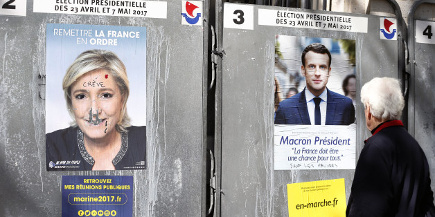 PARIS, FRANCE - APRIL 19: A pedestrian looks at official campaign posters of Marine Le Pen, French National Front (FN) and political party leader and an official poster of Emmanuel Macron, head of the political movement En Marche! (On move !), two of the eleven candidates who runs in the 2017 French presidential election on April 19, 2017 in Paris, France. Le Pen and Macron are candidates for the France's 2017 presidential elections and polls predict their presence in the second round of this e