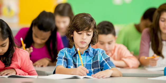 A multi-ethnic group of elementary age children are sitting at their desks are are writing in their notebooks.