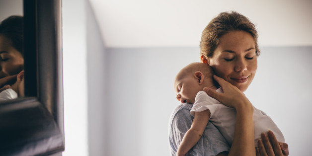 A happy new mother smiles as she craddles her sleeping baby in her arms. She has her eyes closed as she holds her close.