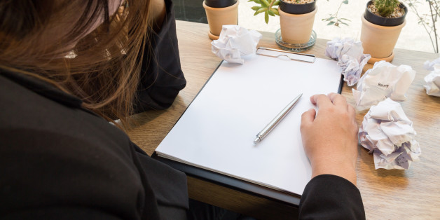 Stressed woman sitting at wooden desk with paper balls.