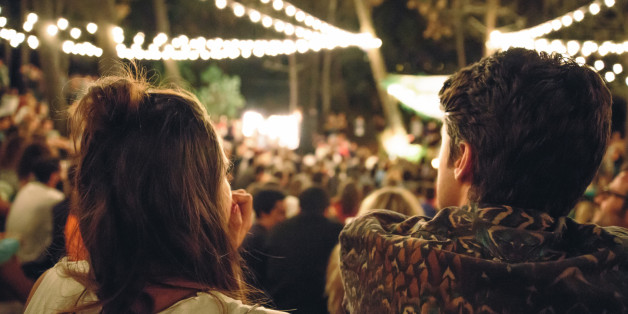 Back view of young couple sitting and enjoying in a open night music festival outdoors on summer