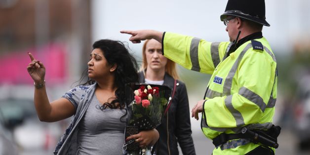 A police officer (R) directs a woman carrying a bunch of flowers near the Manchester Arena in Manchester, northwest England on May 23, 2017 following a deadly terror attack at the concert at the venue the night before. Twenty two people have been killed and dozens injured in Britain's deadliest terror attack in over a decade after a suspected suicide bomber targeted fans leaving a concert of US singer Ariana Grande in Manchester. / AFP PHOTO / Oli SCARFF (Photo credit should read OLI SCAR