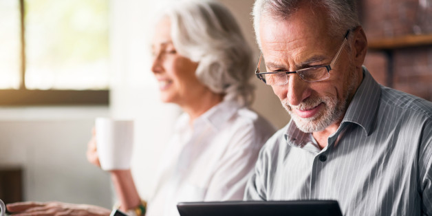 Daily life. Old grey man in glasses using laptop while woman drinking tea and smiling