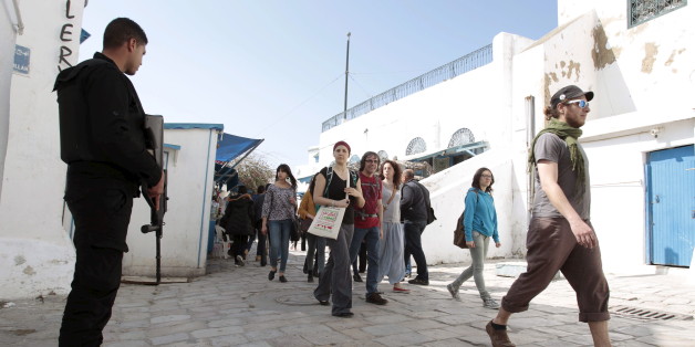 A police officer (L) stands guard as tourists walk in Sidi Bou Said, a tourist destination, in Tunis March 23, 2015.Tunisian Prime Minister Habib Essid fired six police commanders on Monday, including the head of tourist security, after a militant attack on Bardo national museum last week in which 20 foreign visitors were killed. REUTERS/Zoubeir Souissi