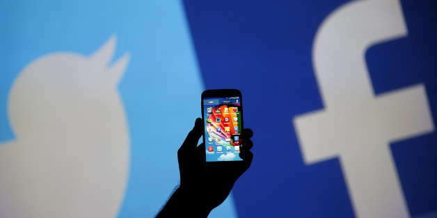A man holds up a Samsung S4 smartphone against a video screen with Twitter and Facebook logos in this photo illustration taken in the central Bosnian town of Zenica, August 14, 2013. REUTERS/Dado Ruvic (BOSNIA AND HERZEGOVINA - Tags: BUSINESS TELECOMS)