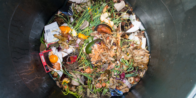 Photo of a plastic home composting bin with freshly intorduced kitchen scraps and other biodegradable matter on top. Composting is a way to recycle food and garden waste at home. The compost can be used as a garden fertilizer.