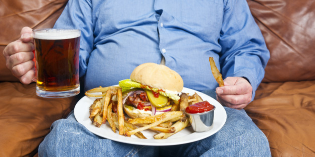 A photo of an overweight man sitting on an old couch with a very large unhealthy meal on his lap and a pint of beer in his hand. Obesity is a major cause of diabetes.