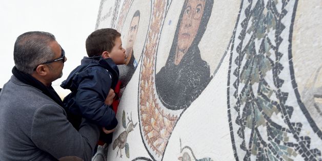 TOPSHOT - Mohamed, the son of Tunisian policeman Aymen Morjane who got killed last year in a jihadist assault on the Bardo museum, kisses a memorial bearing the portrait of his father outside the museum in Tunis on March 18, 2016, as the country marks the first anniversary of the attack. / AFP / FETHI BELAID (Photo credit should read FETHI BELAID/AFP/Getty Images)