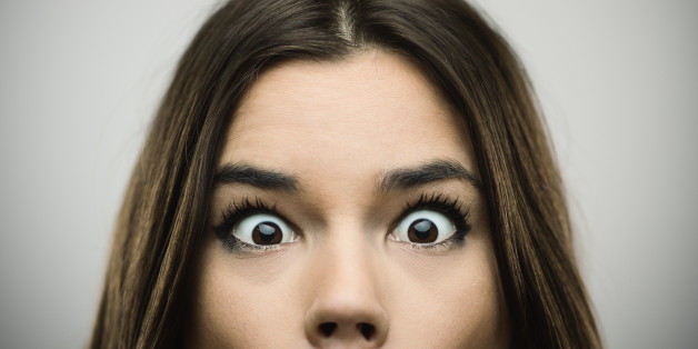 Close-up portrait of happy young woman with surprised face. Cheerful female is against gray background. Horizontal studio photography from a DSLR camera. Sharp focus on eyes.