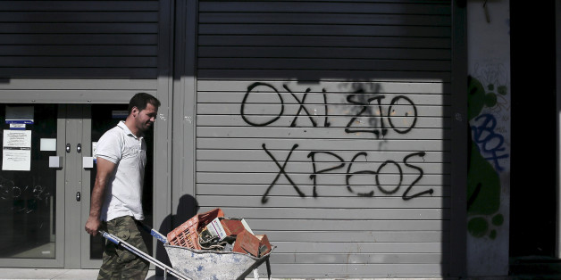Graffiti on a closed Attica Bank branch reads "No to the debt" as a worker pushing a cart walks by in Athens, Greece July 13, 2015. REUTERS/Alkis Konstantinidis/File photo