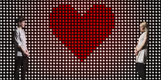 young couple in front of light wall, with huge heart made of red dots, dating