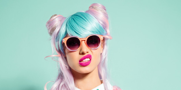 Portrait of manga style blue-pink hair girl wearing sunglasses and pink polka dot dress with collar and bow tie. Standing against turquoise background, looking at camera. Studio shot, one person.