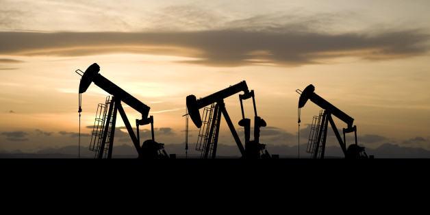 Three oil and gas industry derricks work as the sun sets behind them.