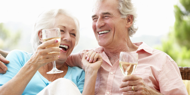 Senior Couple Sitting On Outdoor Seat Together Drinking Wine Laughing