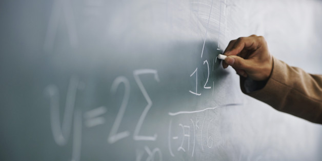 Cropped image of a teacher writing a formula on a blackboard