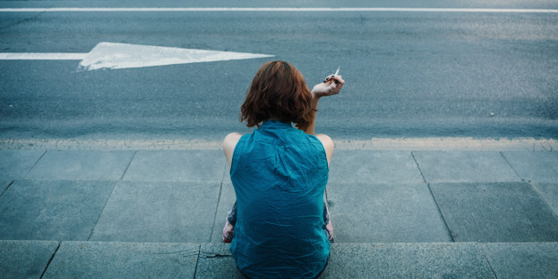 Teenage girl smoking on a sidewalk near the boulevard.