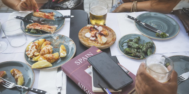 Tourists in Barcelona eating tapas in a typical restaurant in the Barri Gotic. On the table a travel guide of Spain and a smartphone.