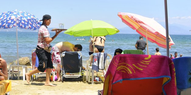 A beach attendant carries a tray of refreshments to holidaymakers at a tourist resort in Stavros, Greece, on Sunday, July 12, 2015. Tourism is the main source of earnings for debt-ravaged Greece, accounting for about 17 percent of the economy. Photographer: Oliver Bunic/Bloomberg via Getty Images