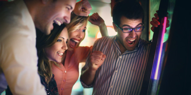 Group of young adults gambling in casino and having major fun.Playing frutties on slot machine.One opf the girls is on the move,rest are cheering for her.Two couple on double date.