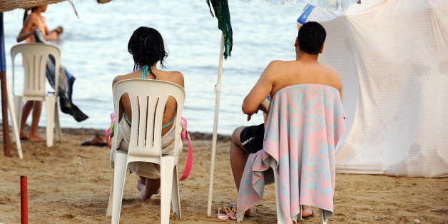 A Tunisian couple sits on the beach in la Goulette city on July 11, 2012 in Tunis as temperatures reached over 45 degreees Celcius over the week in Tunisia. Women and girls who used to swim in bikinis are scarce. Fearing possible attacks by organized religious extremists, they avoid these beaches. AFP PHOTO : FETHI BELAID (Photo credit should read FETHI BELAID/AFP/GettyImages)
