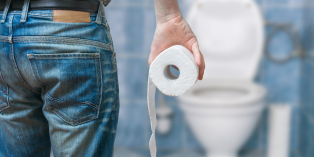 Man suffers from diarrhea holds toilet paper roll in front of toilet bowl.