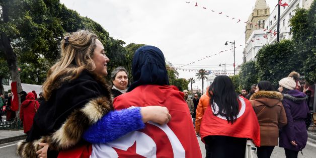 Two Tunisian women embrace as one wears the national flag, during a rally on January 14, 2017 in the Habib Bourguiba Avenue in the capital Tunis to mark the sixth anniversary of the 2011 revolution. / AFP / FETHI BELAID (Photo credit should read FETHI BELAID/AFP/Getty Images)
