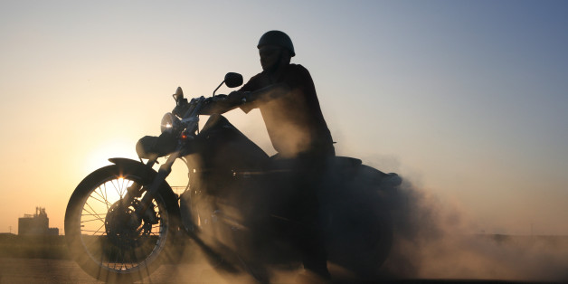 Silhouette of motorcycle and rider against blue prairie sky. Sunlight casts gorgeous shadows through wheel spokes, while smoke from burning tire billows behind bike