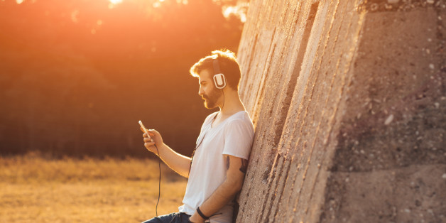 Hipster boy leaning on a wall and listening to music on his mobile phone