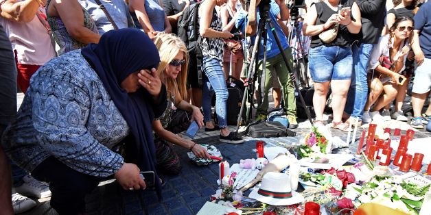 People gather next to flowers, candles and other items set up on the Las Ramblas boulevard in Barcelona as they pay tribute to the victims of the Barcelona attack, a day after a van ploughed into the crowd, killing 13 persons and injuring over 100 on August 18, 2017.Police hunted for the driver who rammed a van into pedestrians on an avenue crowded with tourists in Barcelona, leaving 13 people dead and more than 100 injured, just hours before a second assault in a resort along the coast. / AFP