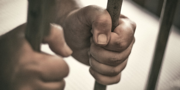 Man's hands tightly holding the bars of his jail cell.