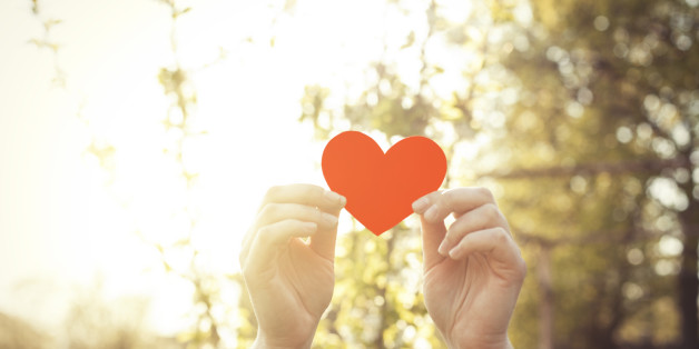 Woman hand holding heart shape against beautiful spring bokeh background