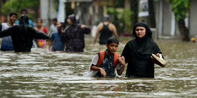 An Indian woman wades with her son through flooded street during heavy rain showers in Mumbai on August 29, 2017.Heavy rain brought India's financial capital Mumbai to a virtual standstill on August 29, flooding streets, causing transport chaos and prompting warnings to stay indoors. Dozens of flights and local train services were cancelled as rains lashed the coastal city of nearly 20 million people. / AFP PHOTO / PUNIT PARANJPE (Photo credit should read PUNIT PARANJPE/AFP/Getty Images)
