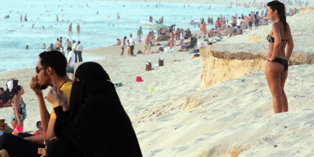 TO GO WITH AFP STORY EMAN MOHAMMED
A foreign woman wearing a bikini stands near an Emirati couple on a beach in Dubai on May 21, 2012. The UAE may be the Gulf's most liberal Arab state but two local women have caused a stir with an online campaign against the 'repulsive' habit of Western women to reveal too much flesh in public. AFP PHOTO/KARIM SAHIB (Photo credit should read KARIM SAHIB/AFP/GettyImages)