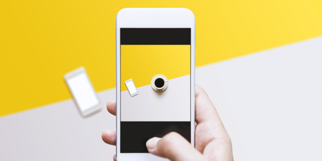 Coffee in white cup and blank screen white phone on white yellow color block background. Top view shot. Hand photographing food on color block background with mobile phone.
