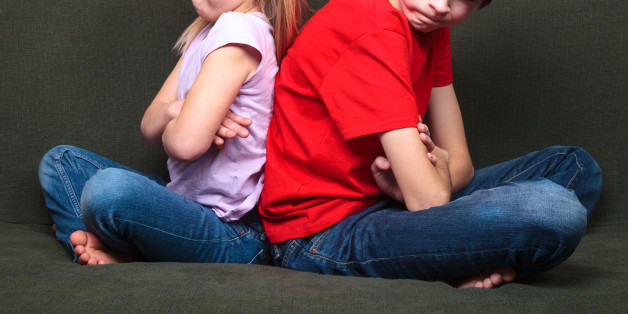 Brother and sister wearing casual clothes sitting on a green sofa at home arms crossed back to back angry with each other