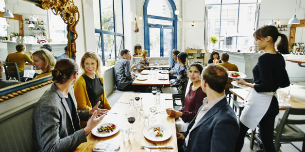 Waitress delivering food to group of friends dining together at table in restaurant