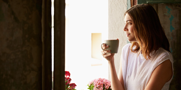 Shot of a young woman drinking a cup of coffee while looking out of a window