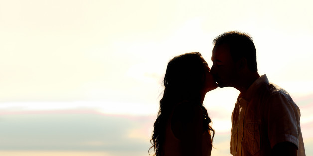 Silhouette of romantic young couple kissing at sunset backlit