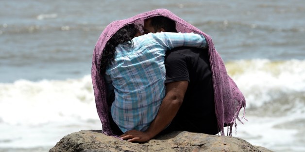 A young couple sit together on a rocky outcrop off the Arabian sea in Mumbai on July 3, 2015. AFP PHOTO / INDRANIL MUKHERJEE (Photo credit should read INDRANIL MUKHERJEE/AFP/Getty Images)