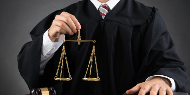 Close-up Of Male Judge Holding Golden Weight Scale At Desk