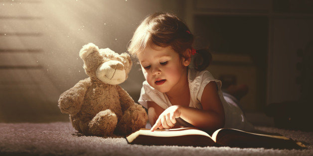 child little girl reading a magic book in the dark home with a toy teddy bear