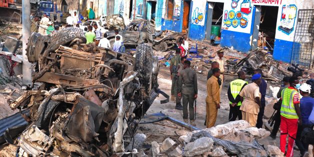 Residents walk at the scene of a blast on October 29, 2017, a day after two car bombs exploded in Mogadishu.Somalia's security ministry said today that forces had killed two gunmen and captured three after a siege at a Mogadishu hotel following a twin car bombing that left at least 14 dead. The attack began when a car bomb exploded outside the hotel entrance, followed by a minibus loaded with explosives going off at a nearby intersection. / AFP PHOTO / Mohamed ABDIWAHAB (Photo credit shou