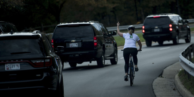 TOPSHOT - A woman on a bike gestures with her middle finger as a motorcade with US President Donald Trump departs Trump National Golf Course October 28, 2017 in Sterling, Virginia. / AFP PHOTO / Brendan Smialowski (Photo credit should read BRENDAN SMIALOWSKI/AFP/Getty Images)