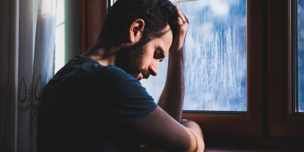 Young sad mad sitting by the window in regret