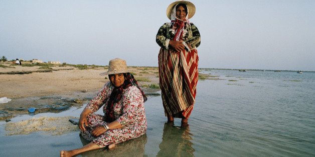 Two washer women draped in colourful gowns by the sea where they work. | Location: Kratten, Chergui, Tunisia. (Photo by In Pictures Ltd./Corbis via Getty Images)