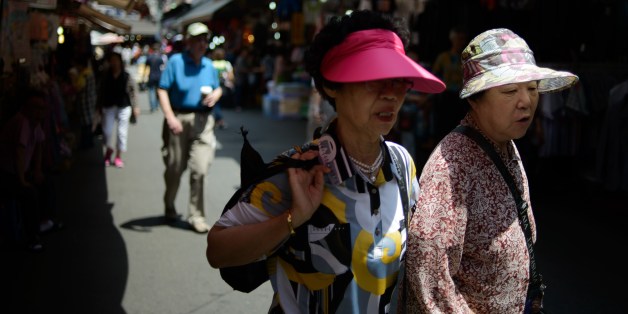 Elderly women wearing sun visors walk in a market in Seoul on May 30, 2014. Sun visors are a familiar sight during the summer months in South Korea, which places a high importance on UV protection and skin care. AFP PHOTO / Ed Jones (Photo credit should read ED JONES/AFP/Getty Images)