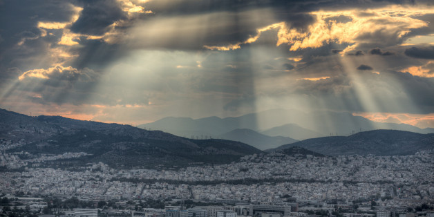 Dramatic sunset with rays of sunlight breaking through dramatic clouds over the city of Athens, Greece.