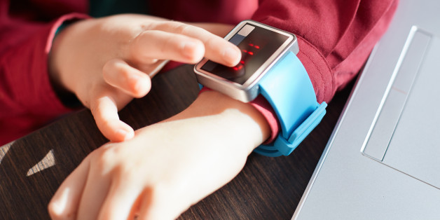 A close-up of child`s hands with smart watch. Touching electronic watch. Wearable gadget concept. Showing time. Using smartwatch while sitting near the laptop. Technology and people concept.