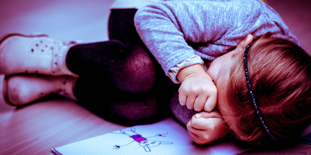 Upset little girl curled up on the bed next to her drawing rubbing her eyes with her fists as though crying, side vignette